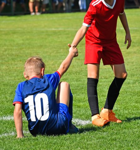 junger Fussballer reicht dem gestürzten Gegner die Hand